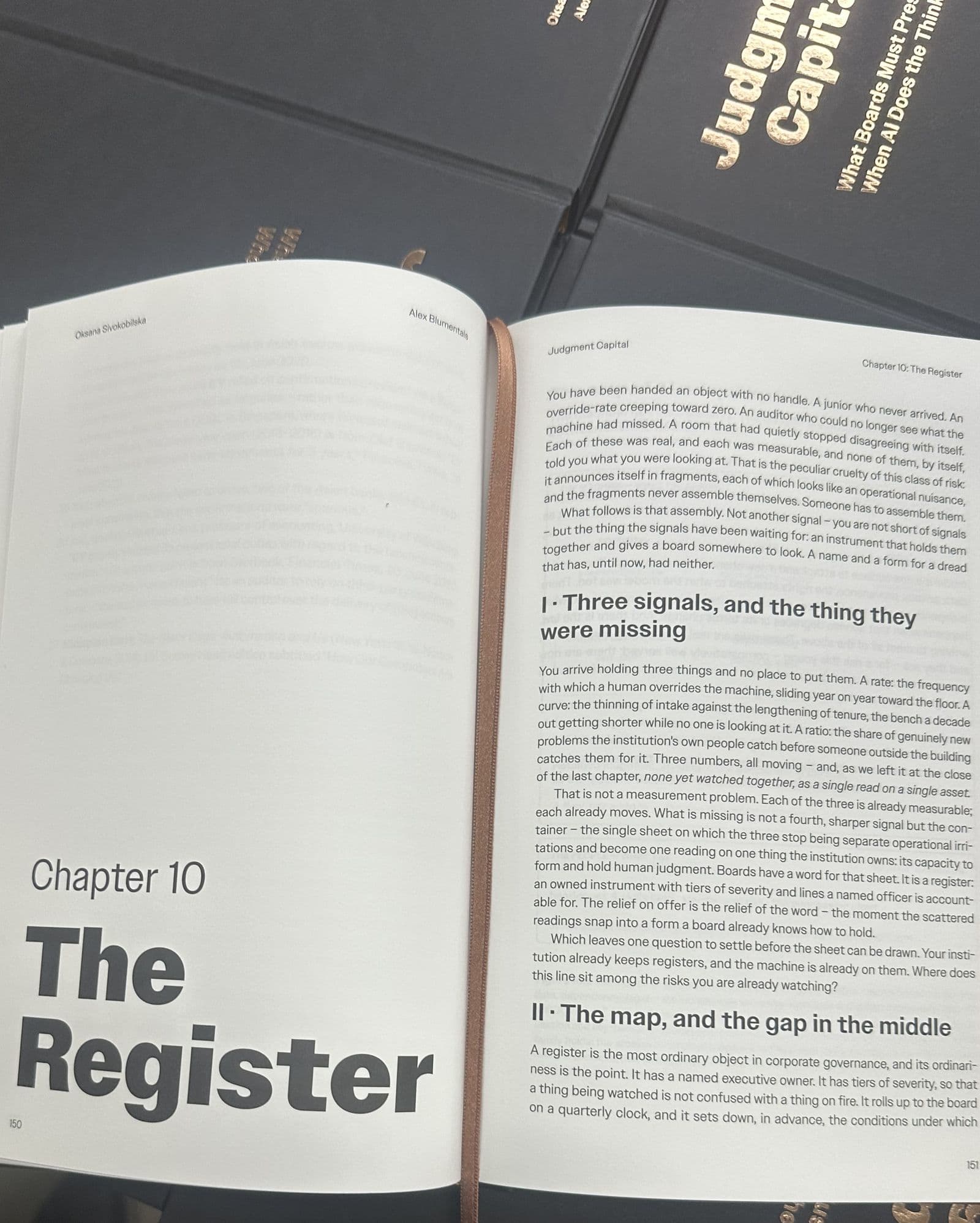 The book open at Chapter 10, The Register, on a stack of copies, with its ribbon marker